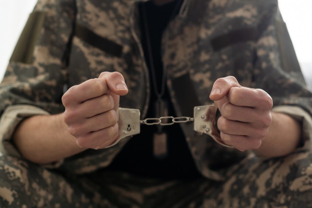 A handcuffed soldier behind the bars against a black background. Concept: court martial, refusal to